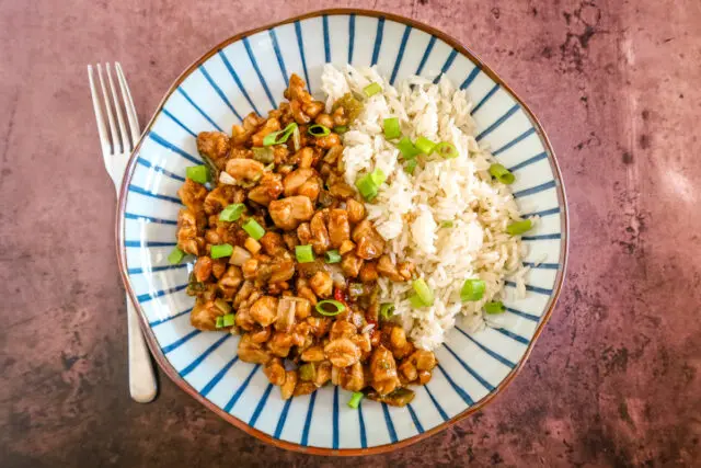 A serving of kung pao chicken with rice and green onion garnish.