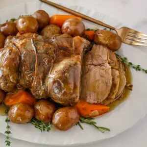 roasted leg of lamb on a platter with vegetables and gravy