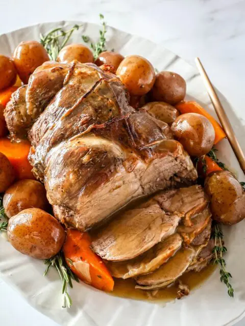 roast leg of lamb with gravy on a platter with vegetables