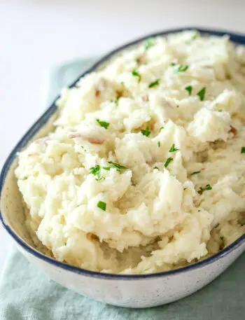 A serving bowl with make-ahead mashed potatoes garnished with parsley.