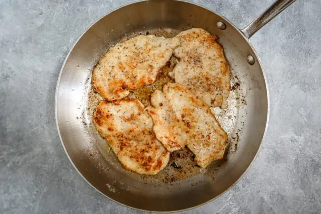 Chicken breasts are dredged in seasoned flour and cooked in a skillet.