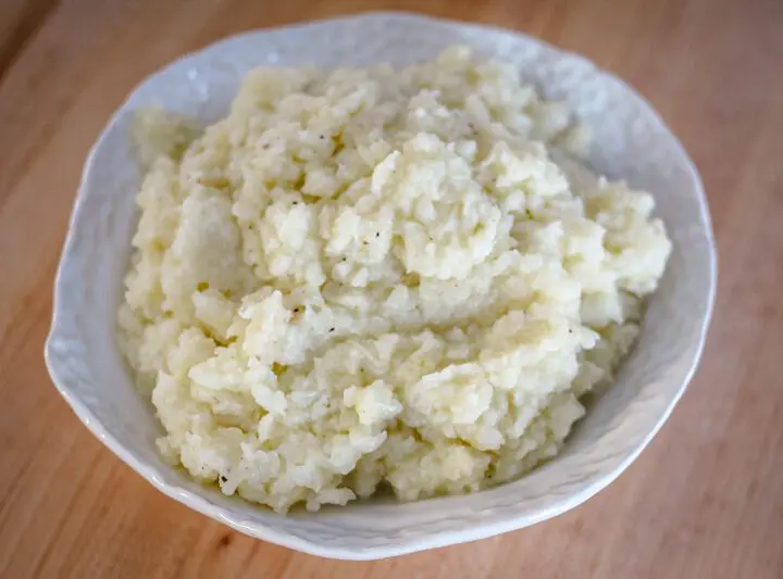 A bowl of fluffy mashed cauliflower made with butter, cream, garlic, and seasonings.