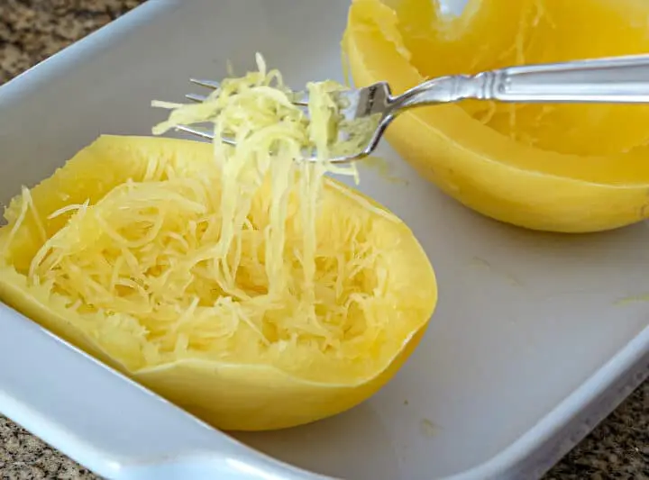 Spaghetti squash in a baking dish cooked in the microwave—strands lifted with a fork.