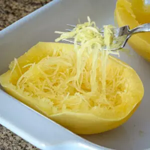 Easy microwave spaghetti squash in the baking dish with a fork separating the strands