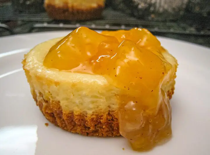 A delicious mini cheesecake on a plate with peach topping.