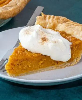 A slice of sweet potato pie on a plate with a dollop of whipped cream and cinnamon sugar.