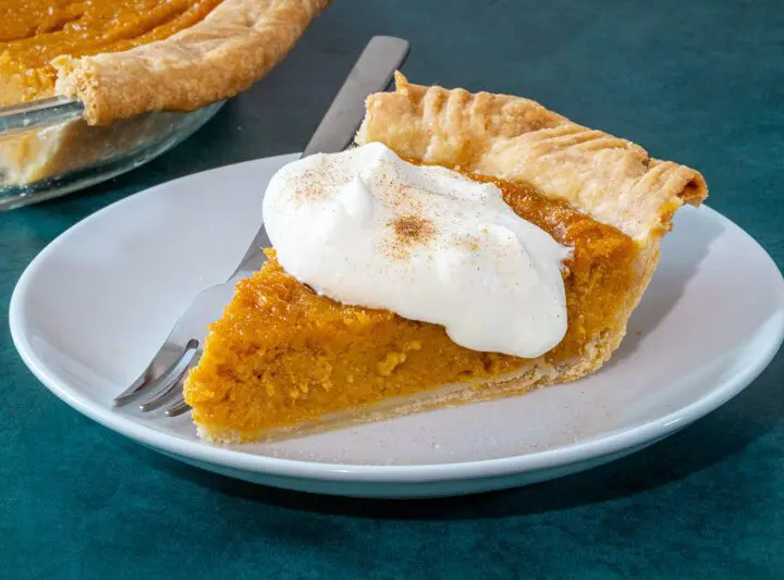 A slice of sweet potato pie on a plate with a dollop of whipped cream and cinnamon sugar.