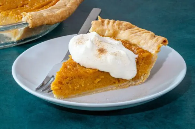 A slice of sweet potato pie on a plate with a dollop of whipped cream and cinnamon sugar.