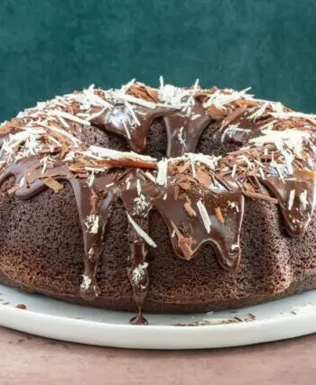 Moist chocolate bundt cake on a plate, decorated with a chocolate glaze and chocolate shards.