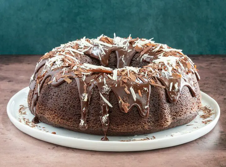 Moist chocolate bundt cake on a plate, decorated with a chocolate glaze and chocolate shards.