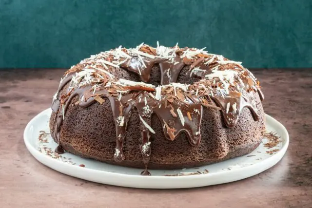 Moist chocolate bundt cake on a plate, decorated with a chocolate glaze and chocolate shards.