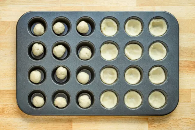 Pressing the dough into the mini muffin tin to make mushroom tarts.