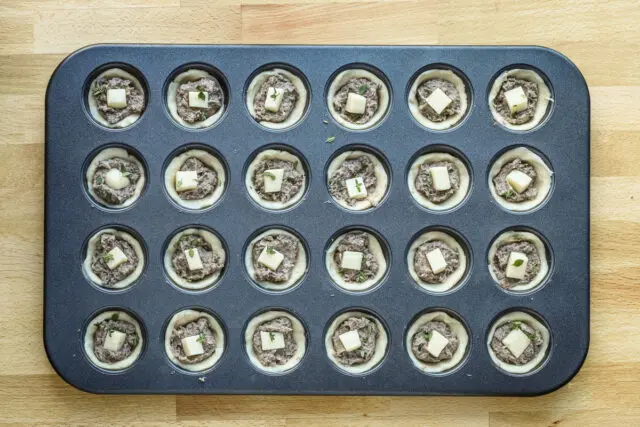 Mushroom tarts with a cube of fontina cheese and thyme, ready to bake.