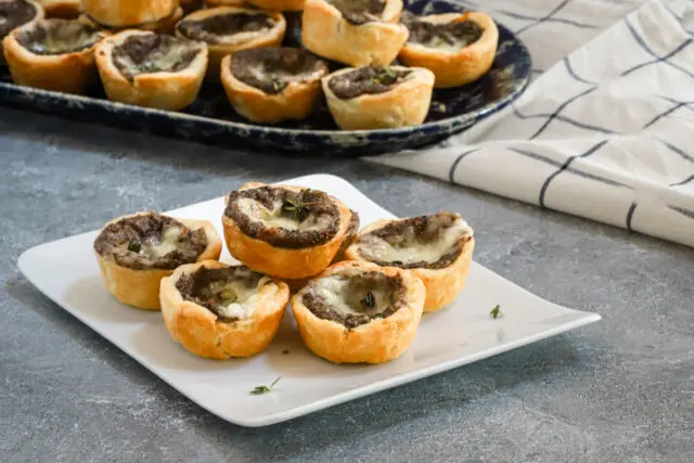 Mushroom tartlets with fontina cheese shown on a serving plate with a tray in the background.