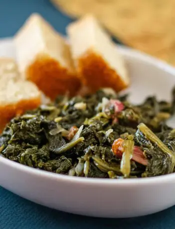 a dish of mustard greens with bacon and sliced cornbread