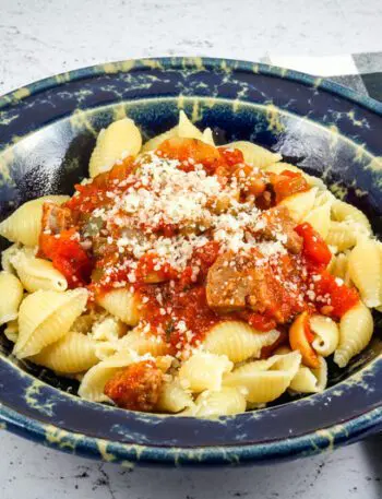 A wide bowl with Neapolitan sauce with sausage and tomatoes over pasta shells.