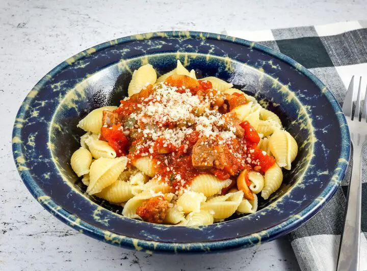 A wide bowl with Neapolitan sauce with sausage and tomatoes over pasta shells.