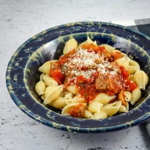 A wide bowl with Neapolitan sauce with sausage and tomatoes over pasta shells.