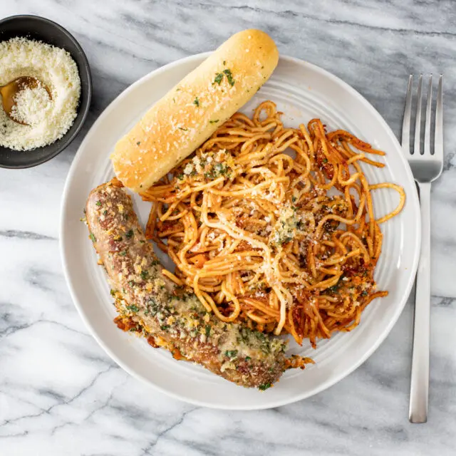 A serving of one pot spaghetti and sausages with a crispy topping and Parmesan cheese on the side.