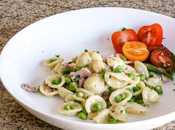 A pasta bowl with a dish of orecchiette with ham, peas, and Parmesan cheese.