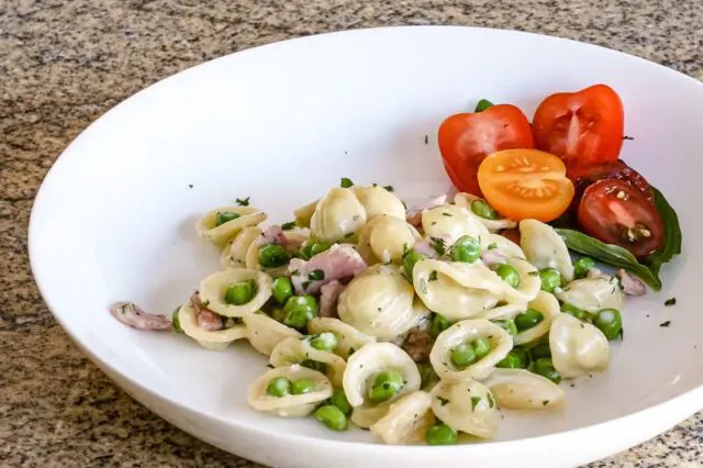 A pasta bowl with a dish of orecchiette with ham, peas, and Parmesan cheese.