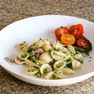 orecchiette with peas and ham in a bowl with some sliced grape tomatoes.