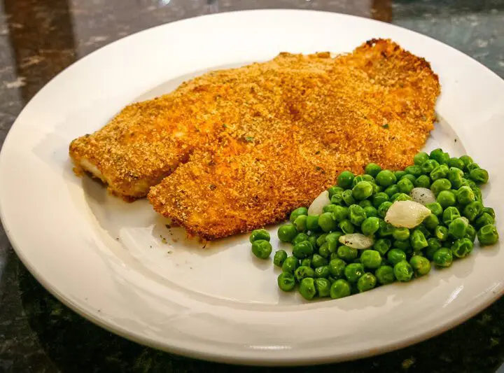 A plate with oven-fried tilapia and peas.