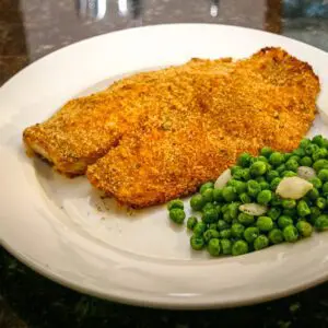 A serving of oven fried tilapia with peas on the side.