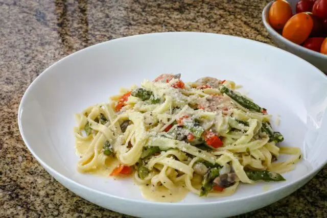 closeup photo of a bowl of pasta with asparagus and ham.