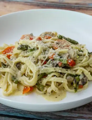 a bowl of pasta with asparagus and ham in a parmesan cheese sauce