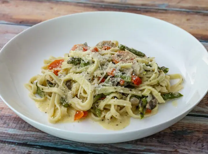 a bowl of pasta with asparagus and ham in a parmesan cheese sauce