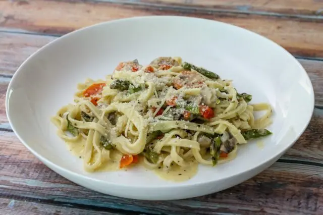 a bowl of pasta with asparagus and ham in a parmesan cheese sauce