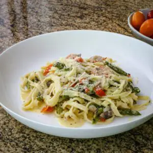 A bowl of pasta with asparagus and ham.