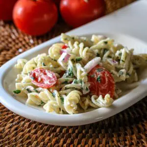 pasta salad on a serving plate with tomatoes and basil