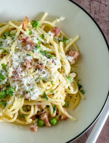 pasta with pancetta and peas on a plate with pecorino romano cheese garnish