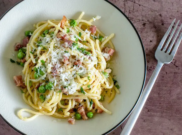 pasta with pancetta and peas on a plate with pecorino romano cheese garnish