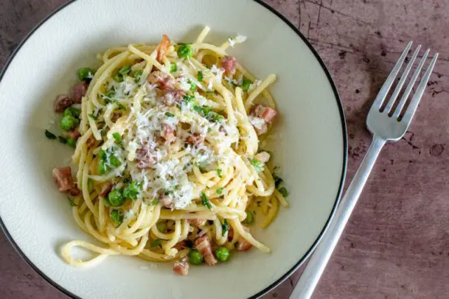 pasta with pancetta and peas on a plate with pecorino romano cheese garnish