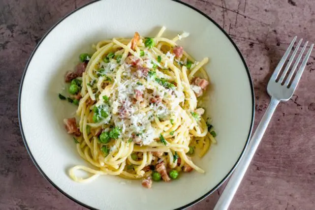 spaghetti with pancetta and peas, garnished with grated pecorino romano cheese