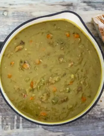 A saucepan with pea soup and crusty bread on the side