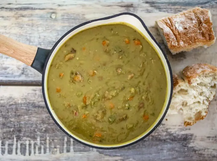 A saucepan with pea soup and crusty bread on the side