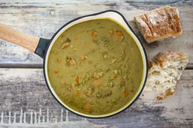 A saucepan with pea soup and crusty bread on the side