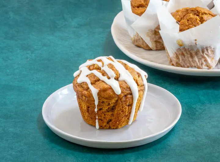 A pumpkin muffin with icing and more pumpkin muffins in the background