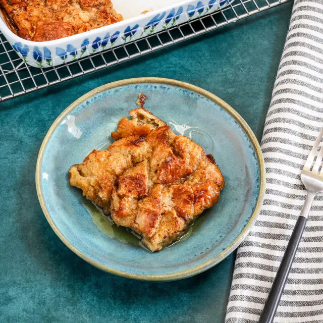 A baked French toast casserole serving with maple syrup and the casserole dish in the background.