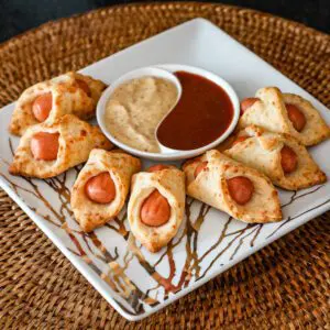 A serving plate with pigs in a blanket and dips.