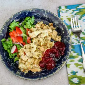 A serving of chicken and dressing casserole on a plate with a side of cranberry sauce.