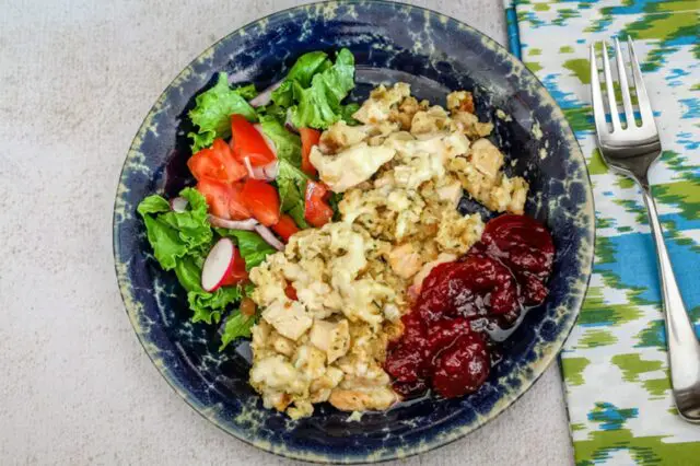 Chicken and dressing portion on a plate with cranberry sauce and a small salad.