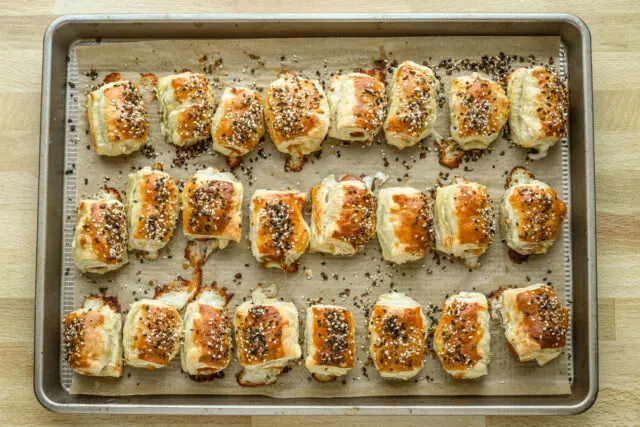 Baked puff pastry pigs in a blanket on the baking sheet.