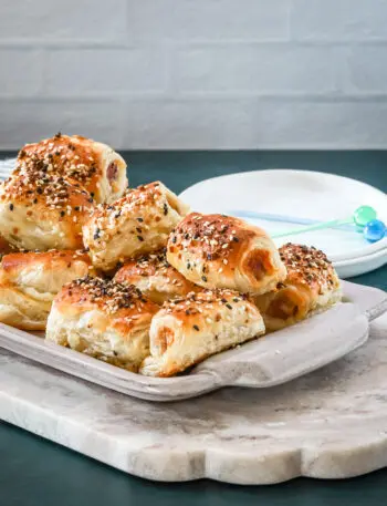 A serving tray with baked puff pastry pigs in a blanket with small appetizer plates and picks for serving.