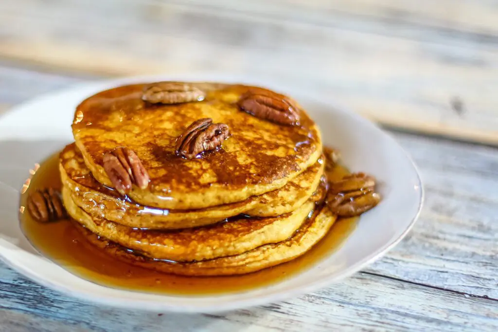 pumpkin pancakes on a plate with toasted pecans and maple syrup