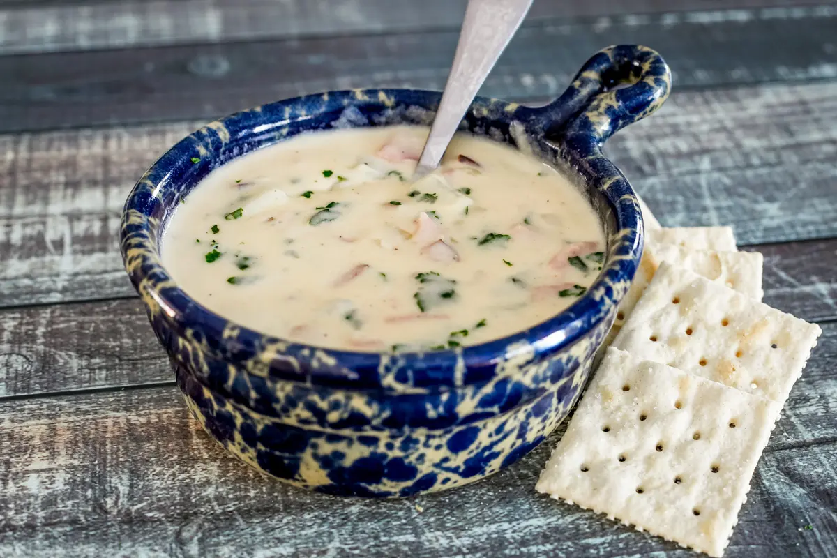 A bowl of potato soup with crackers on the side.